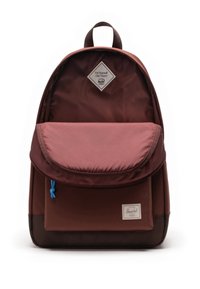 Smeđi platneni ruksak s prednjim džepom, zakrivljenim poklopcem i plavim akcentom od kordele. Ima dijamantni logo i petlju za vješanje na vrhu.