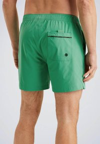 Zelené plavky vyrobené z ľahkého materiálu. Elastický pás s zadnou kapsou, ktorá má kontrastný zips a okrúhly detail očka.