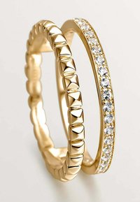 Anillos de oro: uno con un diseño texturizado y con tachuelas, y el otro que presenta una fila de piedras transparentes engastadas en una banda lisa.