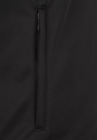 Tessuto nero con una texture liscia che presenta una tasca funzionale con zip sul lato destro, integrata nel design del capo.