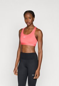 Nike koraalroze sportbeha met een ronde halslijn en brede banden, gecombineerd met zwarte leggings met hoge taille en een klein wit logo.