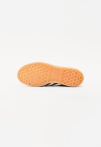 Sola de sapato de borracha com um padrão em colmeia, apresentando um fundo laranja texturizado e riscas pretas. Logótipo estampado no calcanhar.