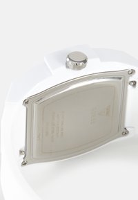 Dos de montre blanc montrant un couvercle en acier inoxydable fixé par quatre vis et une couronne ronde argentée sur le côté.