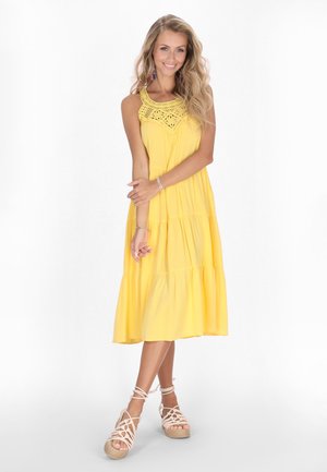 Abito giallo a strati con scollo in crochet. Tessuto leggero, design senza maniche e vestibilità comoda. Abbinato a zeppe in espadrillas color pelle.