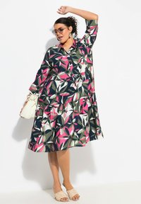 Blommönstrad klänning med en flikad kjol, långa ärmar och knäppning fram. Färgerna inkluderar marinblå, grön, rosa och vit. Bärs med beiga sandaler.