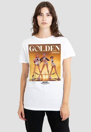 Woman wearing white T-shirt featuring three futuristic female characters with "GOLDEN" text and sunset background on front.