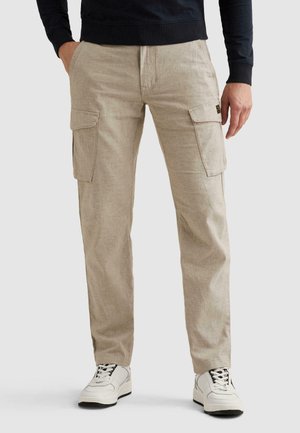 Beige cargobroek met zijflappentassen, gedragen met witte vetersneakers en een zwarte top met lange mouwen.