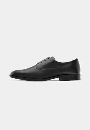 Schwarze Leder-Halbschuh mit schlankem Design, runder Zehenform, fünf Ösen für die Schnürsenkel und einem kleinen, erhöhten Absatz. Dezentes, geprägtes Logodetail.