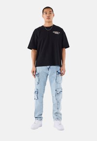 Camiseta de algodón negra oversize con el texto "PROJECT PARIS", combinada con pantalones cargo azul claro que cuentan con múltiples bolsillos y zapatillas blancas.