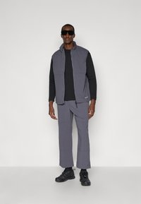 Gray padded vest over a black long-sleeve shirt, paired with gray pants and black athletic shoes. Features include a zippered front and pockets.