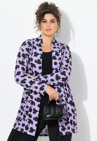 Vaaleanliila neuletakki, jossa on musta kukkakuosi, pitkät hihat, auki edessä ja silkkinen rakenne, yhdistettynä pieneen mustaan käsilaukkuun.