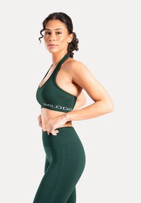 Grönt sportset med en ribbad sport-bh med halterband och höga tights, båda med logotypdetaljer och en slät textur.