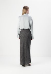 Ljusgrå silkesblus med knapppdetaljer, kombinerad med en lång, mörkgrå randig kjol; outfiten kompletteras med svarta klackar.