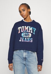 Námornícky skrátený sveter s farebn�ým textom "TOMMY JEANS 1985", s okrúhlym výstrihom a dlhými rukávmi. Nosí sa s svetlými džínsami.