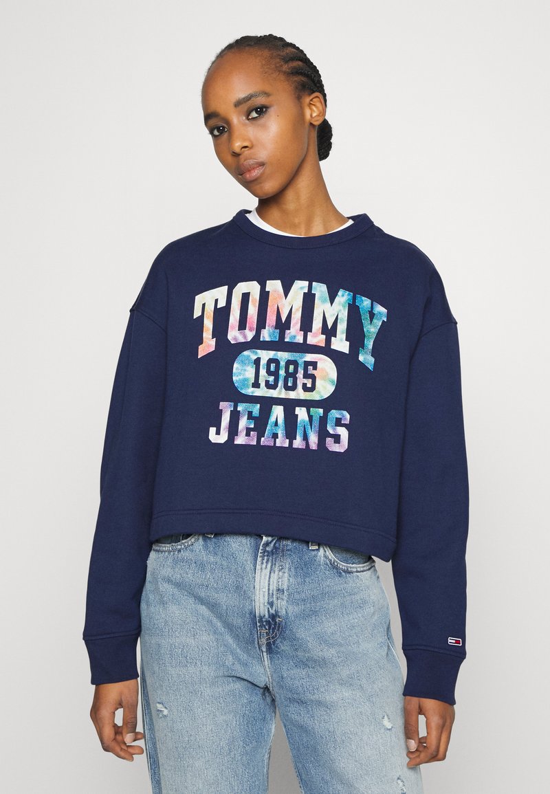 Námornícky skrátený sveter s farebným textom "TOMMY JEANS 1985", s okrúhlym výstrihom a dlhými rukávmi. Nosí sa s svetlými džínsami.