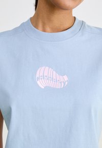 Ljusblå bomullströja med en rosa snäcka grafisk design. Rund halsringning och ärmlös stil. Mjuk textur.