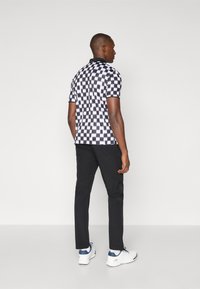 Polo à manches courtes avec un motif en damier noir et blanc, associé à un pantalon noir et des baskets blanches avec des accents bleus.