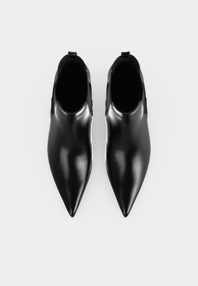 Une paire de bottines en cuir noir à bouts pointus, vues de dessus sur un fond clair.