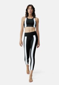 Must ja sportlik crop top valgete vertikaalsete triipudega ja sobivad mustad leggingsid, millel on valged küljepaneelid, on valmistatud venivast ja siledast kangast.