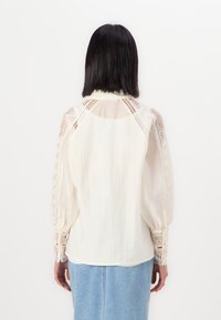 Witte blouse met kantdetails op de mouwen en schouders. Semi-doorzichtige stof, lange pofmouwen en een ontspannen pasvorm.