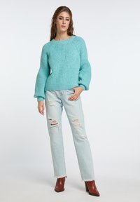 Maglione lavorato a maglia turchese con finitura testurizzata e maniche a sbuffo, abbinato a jeans chiari strappati e stivali con tacco marroni.