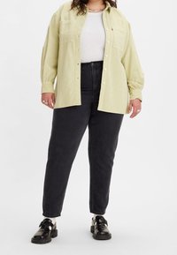 Světlězelená manšestrová košile s předními knoflíky, dvěma kapsami na prsou, doplněná černými džíny s vysokým pasem a černými botami. Viditelná plošná textura.