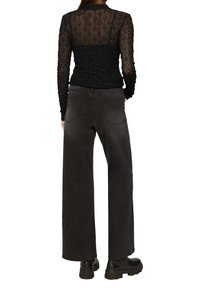 Zwarte kanten lange mouwen top met gerimpelde details, gecombineerd met hoge taille wijde zwarte jeans en chunky zwarte laarzen.