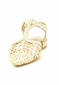 Zapato plano tejido en beige claro y crema con punta afilada y tira en el tobillo. Presenta un tacón bajo y un diseño trenzado texturizado.