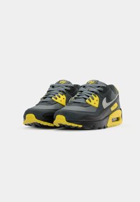 Gray and yellow Nike Air Max 90 sneakers are displayed; features include laces, mesh panels, and air cushioning.
