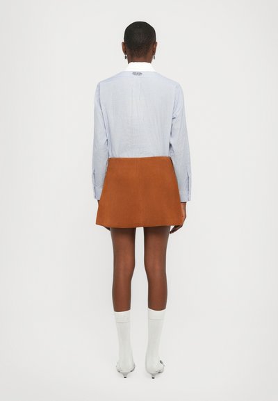 Camicia a maniche lunghe a righe blu e bianche abbinata a una mini gonna in suede beige, che mette in risalto la texture del tessuto e la silhouette snella.
