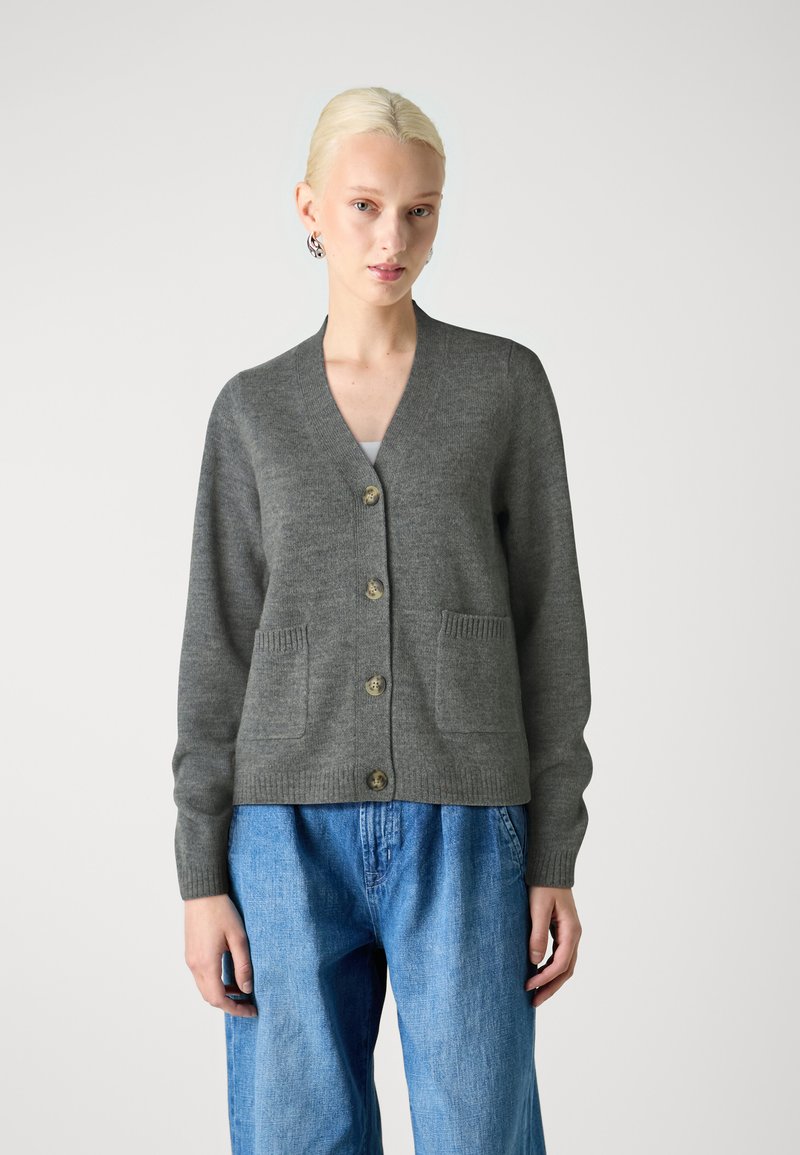 Grå strikket cardigan med V-hals, fire store knapper og to frontlommer. Strukturert stoff med ribbestrikkede mansjetter og kant.
