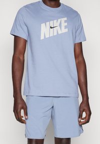 Camiseta Nike de color azul claro con mangas cortas, que presenta un gran logotipo blanco en el pecho y un cuello redondo de tipo crew. Textura de tejido suave.