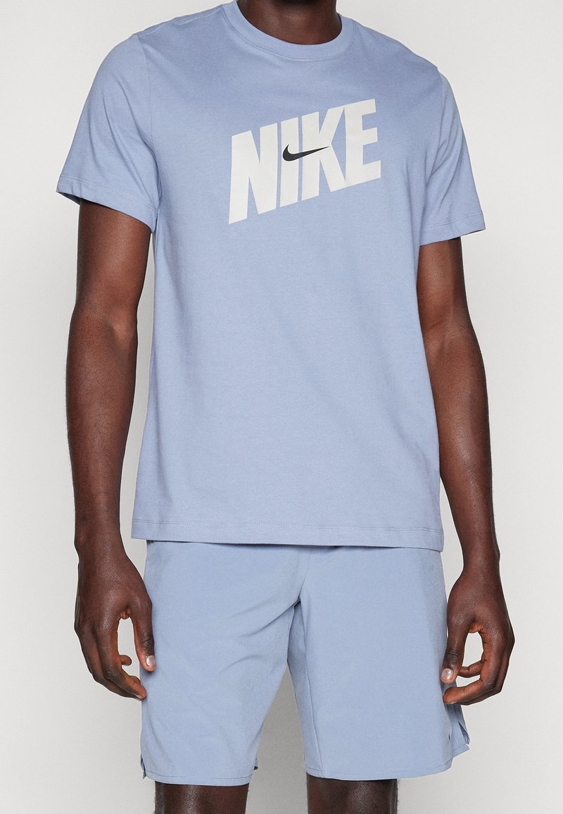 Camiseta Nike de color azul claro con mangas cortas, que presenta un gran logotipo blanco en el pecho y un cuello redondo de tipo crew. Textura de tejido suave.