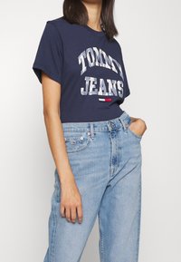 Camiseta azul marino con texto blanco que dice "TOMMY JEANS". Combinada con jeans de tiro alto de color azul claro con el clásico diseño de cinco bolsillos.