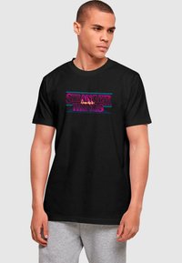 Black cotton t-shirt featuring the text "STRANGER THINGS" in vibrant pink and blue retro font, short sleeves, and a crew neckline.