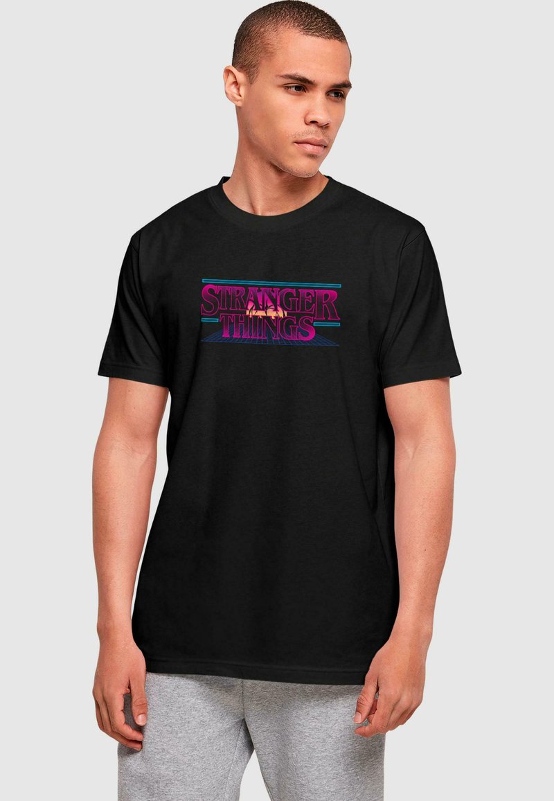 Black cotton t-shirt featuring the text "STRANGER THINGS" in vibrant pink and blue retro font, short sleeves, and a crew neckline.