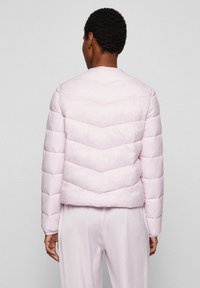 Giubbotto trapuntato rosa chiaro con motivo a chevron e maniche lunghe, caratterizzato da scollo arrotondato e texture liscia.