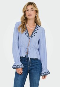 Blauw-wit gestreepte blouse met een v-hals, trekkoorddetails en geborduurde zwarte bloemenpatronen op de mouwen en de zoom. Van katoen.