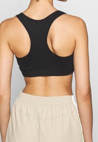 Svart åtsittande sportbh med breda axelband och en slät yta, parat med ljusbeiga shorts med elastisk midja och sidostrick.