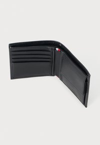 Carteira de couro preta, design dobrável, com vários compartimentos para cartões, textura suave e um pequeno detalhe em vermelho, branco e azul na borda.