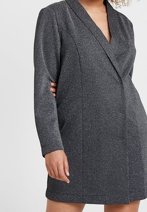 Woman wearing a fitted, long-sleeve, dark gray blazer dress with subtle textured fabric and a deep V-neckline.