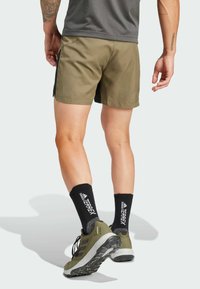 Pantalones cortos deportivos verdes con un diseño elegante, que cuentan con bolsillos laterales. Combinados con calcetines Terrex negros y zapatillas de trail running verdes con suelas texturizadas.