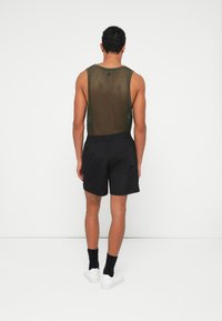 Green mesh tank top with a loose fit, paired with black shorts and white sneakers. Features elastic waistband and minimal hardware accents.