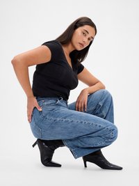 Jeans azules de talle alto con un corte holgado, combinados con una blusa negra ajustada de manga corta y botas de tobillo negras con punta. Texturas suaves en todo.