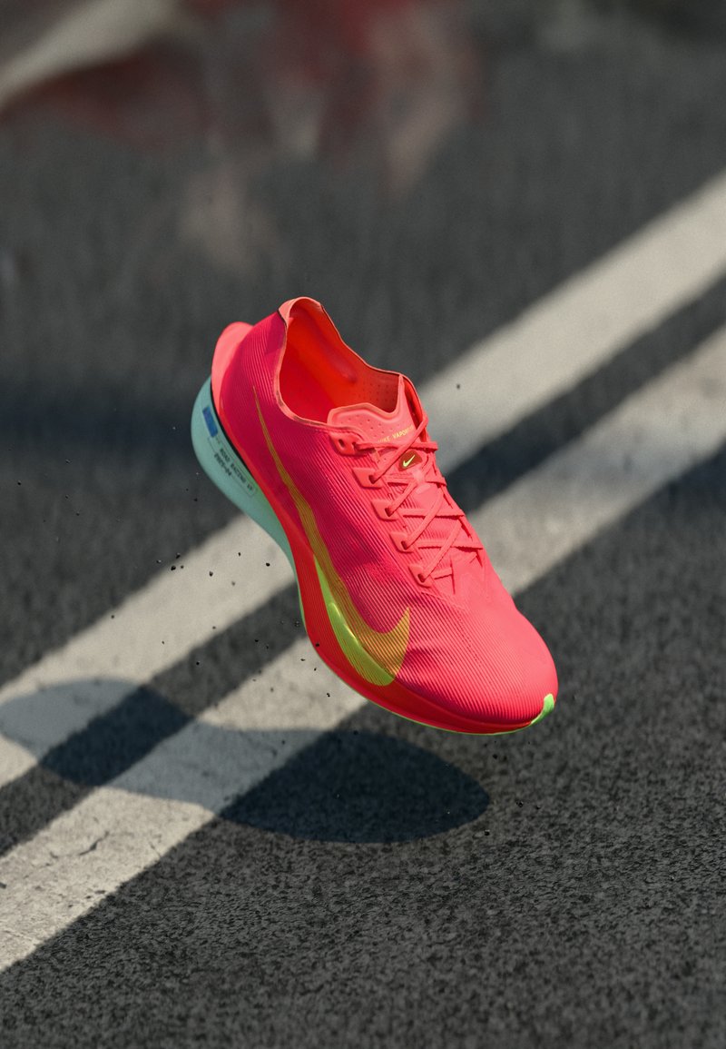 Chaussure de course rose vif avec une tige texturée, des accents jaunes et une semelle légère, montrant un léger rebond sur une surface sombre.