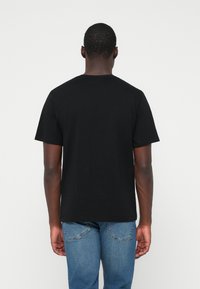 Μαύρη βαμβακερή μπλούζα μ ε κοντά μανίκια, στρογγυλή λαιμόκοψη και χαλαρή γραμμή, εικονίζεται από πίσω μαζί με μπλε τζην παντελόνι.