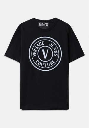 Svart bomulls T-skjorte med korte ermer, med et stort rundt hvitt logo som har teksten "VERSACE JEANS COUTURE" og et sentralt 'V'-design.