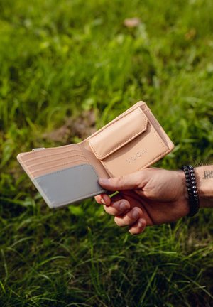 Light tan wallet with multiple card slots and a gray accent. Features a snap closure and embossed logo, displayed open in a hand.