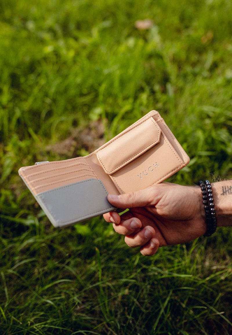 Light tan wallet with multiple card slots and a gray accent. Features a snap closure and embossed logo, displayed open in a hand.