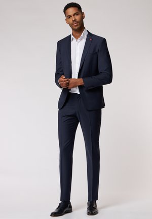Navy check suit with slim fit design, single-breasted jacket, and notch lapels. White shirt underneath, paired with black dress shoes.